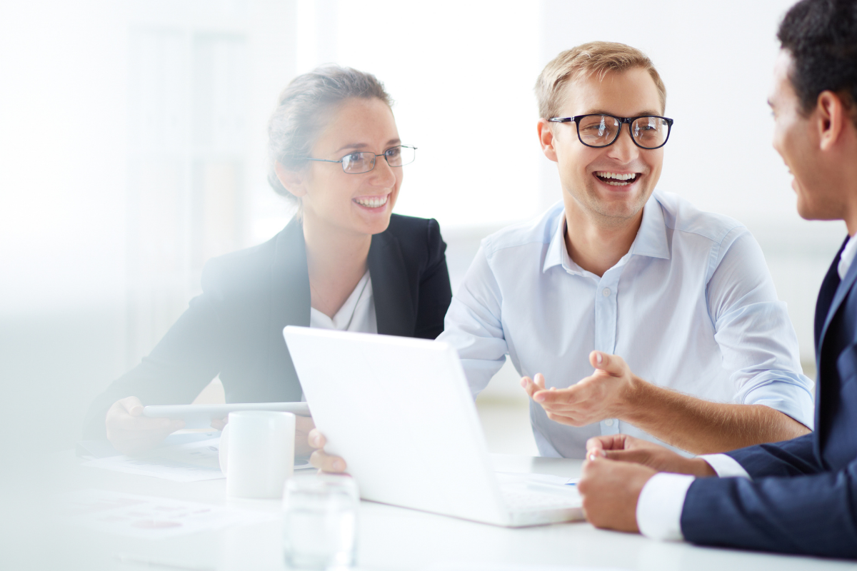 Group of businessmen and woman smile as they are sat around a laptop